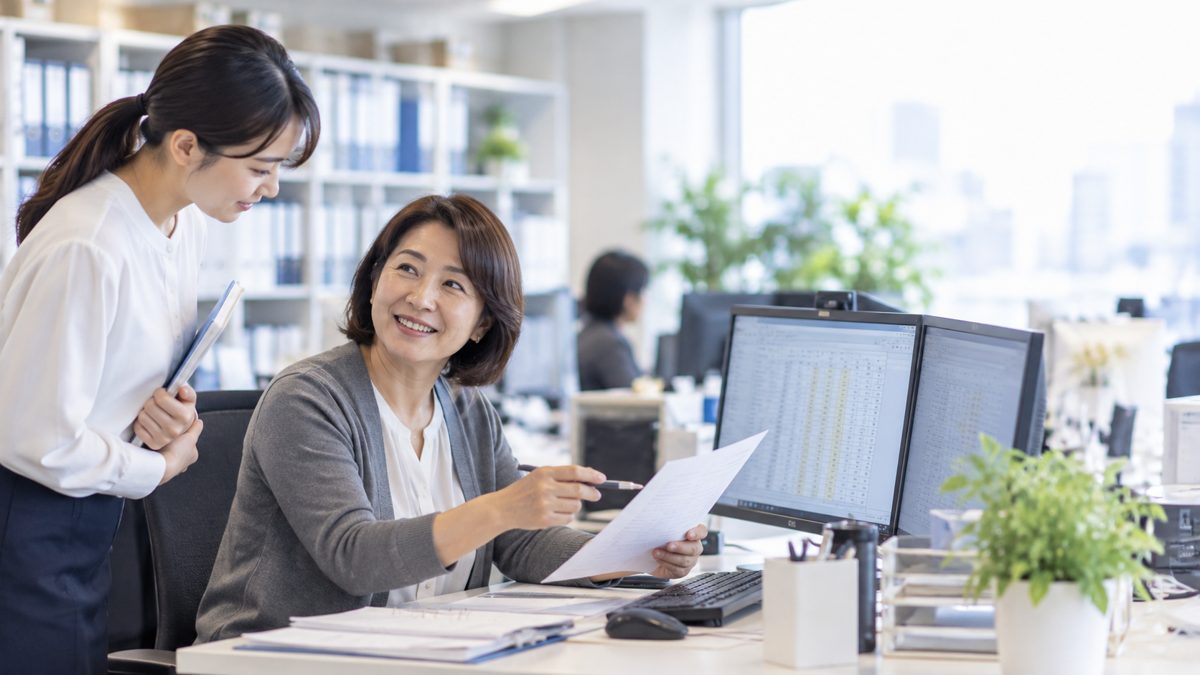 オフィスで若手に書類を説明するベテラン女性社員